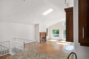 Living room featuring wood finished floors, a fireplace with flush hearth, high vaulted ceiling, recessed lighting, and a skylight