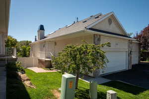 View of side of home with stucco siding, a chimney, an attached garage, and roof with shingles