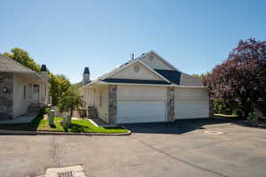 View of front of property featuring asphalt driveway, stucco siding, stone siding, and an attached garage