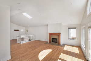 Unfurnished living room with vaulted ceiling, light wood finished floors, a skylight, a fireplace with flush hearth, and recessed lighting