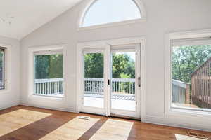 Doorway to outside with vaulted ceiling, plenty of natural light, and wood finished floors