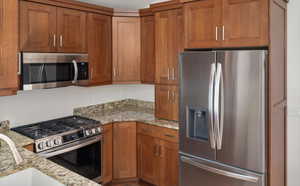 Kitchen featuring stainless steel appliances, brown cabinetry, and light stone counters