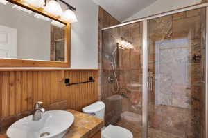 Full bathroom with a stall shower, a wainscoted wall, vaulted ceiling, and wood walls