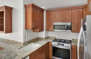Kitchen with stainless steel appliances, light stone countertops, and brown cabinets
