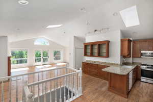 Kitchen with a skylight, brown cabinets, light wood-type flooring, stainless steel appliances, and light stone counters