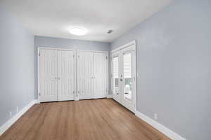 Unfurnished bedroom with multiple closets, wood finished floors, french doors, and access to exterior