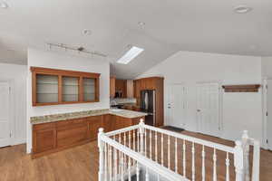 Kitchen with brown cabinets, a skylight, lofted ceiling, light wood-style floors, and glass insert cabinets