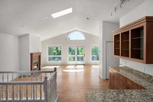 Kitchen featuring a skylight, light wood-type flooring, light stone counters, a premium fireplace, and high vaulted ceiling