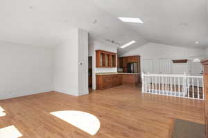 Unfurnished living room with vaulted ceiling, a skylight, light wood-style floors, and recessed lighting