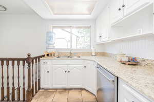 Kitchen with white cabinets, dishwasher, light tile patterned flooring, and light stone countertops