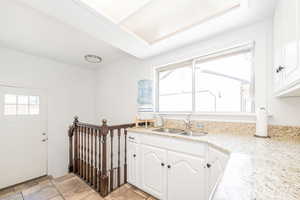 Kitchen with healthy amount of natural light, white cabinets, light stone counters, and light tile patterned floors