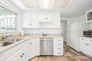 Kitchen featuring white cabinets, stainless steel appliances, light stone countertops, glass insert cabinets, and light tile patterned floors