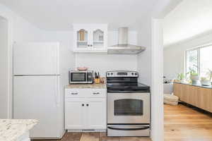 Kitchen featuring white cabinets, appliances with stainless steel finishes, wall chimney exhaust hood, light stone counters, and a textured ceiling