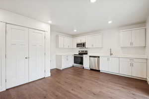 Kitchen with stainless steel appliances, light countertops, recessed lighting, dark wood-type flooring, and white cabinetry