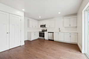 Kitchen with stainless steel appliances, light countertops, dark wood-type flooring, white cabinetry, and recessed lighting