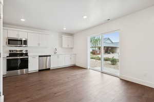 Kitchen with stainless steel appliances, light countertops, dark wood-style flooring, recessed lighting, and white cabinetry