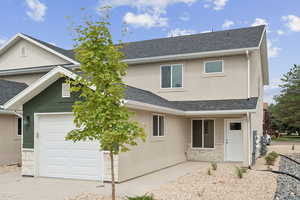 Traditional home with stucco siding, a shingled roof, stone siding, and a garage