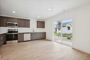 Kitchen featuring stainless steel appliances, dark brown cabinetry, modern cabinets, light wood finished floors, and recessed lighting