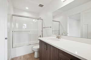Bathroom featuring light wood-type flooring, shower / bath combination with glass door, vanity, and recessed lighting