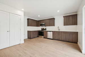 Kitchen featuring dark brown cabinetry, light countertops, stainless steel appliances, light wood-style floors, and recessed lighting