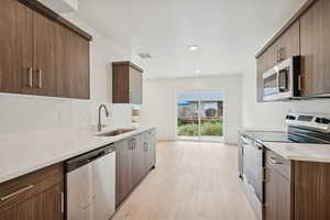 Kitchen with appliances with stainless steel finishes, light stone counters, light wood-type flooring, modern cabinets, and dark brown cabinetry