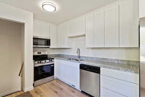 Kitchen with stainless steel appliances, white cabinetry, light stone counters, and light wood-style flooring