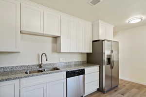 Kitchen featuring white cabinetry, light stone countertops, dishwasher, and light wood-type flooring