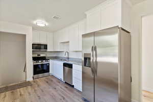 Kitchen with appliances with stainless steel finishes, white cabinets, light wood finished floors, and light stone counters