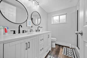 Bathroom with baseboard heating, double vanity, and dark wood-type flooring