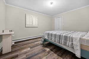 Bedroom featuring baseboard heating, dark wood finished floors, crown molding, and a closet