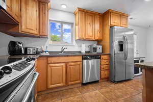 Kitchen featuring stainless steel appliances, dark tile patterned flooring, brown cabinetry, and dark stone counters