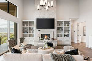 Living area with a high ceiling, a stone fireplace, wood finished floors, and a chandelier