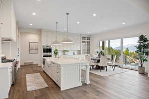 Kitchen featuring a mountain view, an island with sink, pendant lighting, dark wood-type flooring, and light stone counters