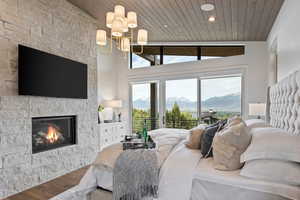 Bedroom with wood finished floors, a stone fireplace, wooden ceiling, access to outside, and a mountain view