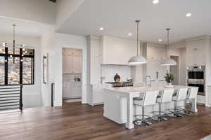 Kitchen featuring decorative light fixtures, a kitchen bar, double oven, a center island with sink, and backsplash