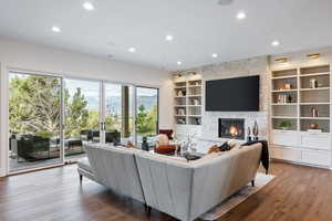 Living area with recessed lighting, a stone fireplace, wood-type flooring, and built in shelves