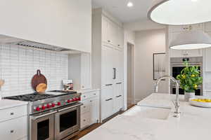 Kitchen with backsplash, appliances with stainless steel finishes, custom exhaust hood, white cabinets, and light stone countertops