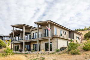 Back of house featuring stone siding, a patio area, and a balcony