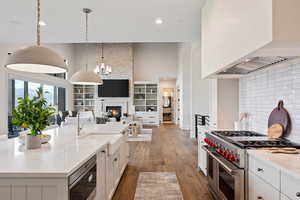 Kitchen featuring appliances with stainless steel finishes, light stone counters, a large fireplace, a high ceiling, and backsplash