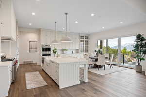 Kitchen with a mountain view, a kitchen island with sink, pendant lighting, recessed lighting, and dark wood-style floors