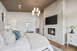 Bedroom featuring wood finished floors, a stone fireplace, a chandelier, connected bathroom, and recessed lighting