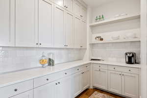 Kitchen with open shelves, light stone counters, white cabinetry, dark wood-type flooring, and tasteful backsplash