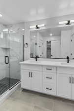 Bathroom featuring double vanity, a marble finish shower, light tile patterned floors, and a textured ceiling