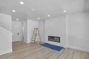 Unfurnished living room featuring a glass covered fireplace, light wood-type flooring, recessed lighting, and a textured ceiling