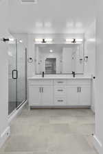 Bathroom featuring double vanity, a marble finish shower, and light tile patterned flooring