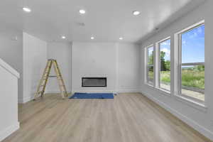 Unfurnished living room with light wood finished floors, recessed lighting, a glass covered fireplace, and a textured ceiling