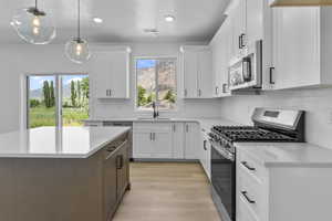 Kitchen featuring stainless steel appliances, white cabinetry, hanging light fixtures, light stone countertops, and light wood-style flooring