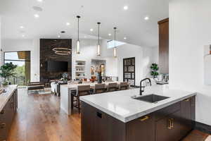 Kitchen with dark brown cabinetry, light stone countertops, decorative light fixtures, light wood-style flooring, and a towering ceiling
