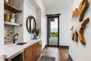 Indoor wet bar with brown cabinetry, backsplash, light wood finished floors, wine cooler, and open shelves