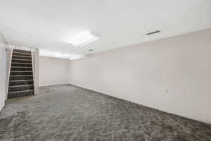 Finished basement with dark carpet, a textured ceiling, and stairs